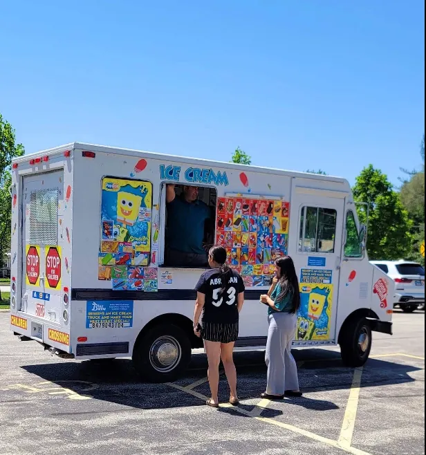 Two guests waiting at the service window of the Yummy Ice Cream Truck on a clear summer day.
